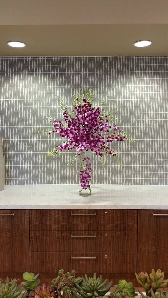 Purple floral arrangement in a vase on a white countertop against a tiled wall.
