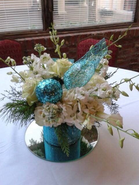 White floral centerpiece with a glittery blue bird decoration in a mirrored vase on a table