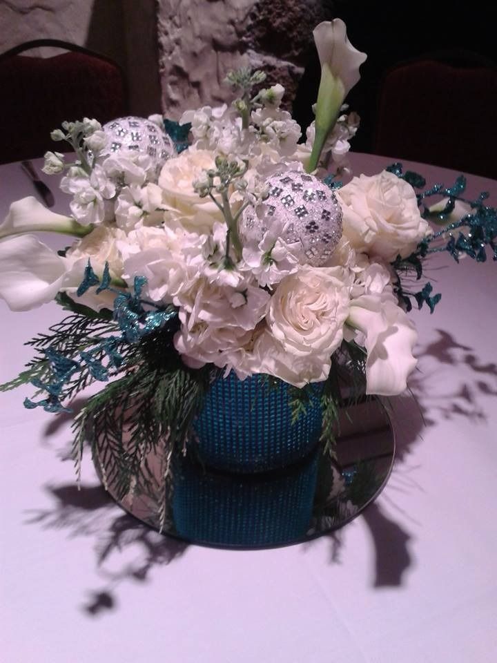 White and blue floral arrangement in a teal vase on a reflective table