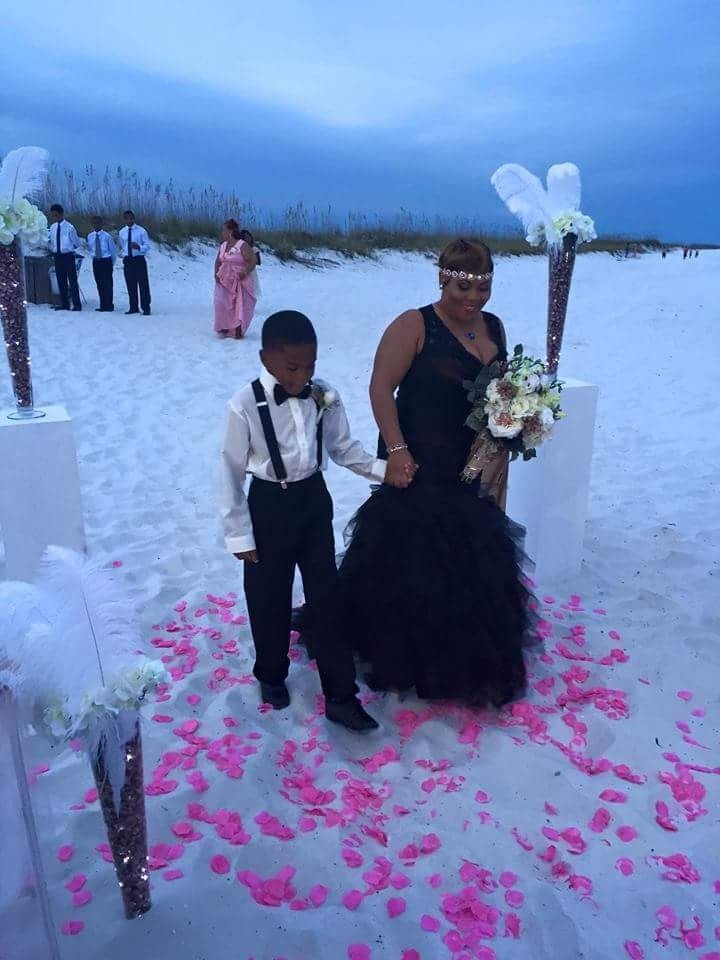 Two people posing on a snow-covered aisle with pink rose petals and white floral decor at an outdoor wedding.