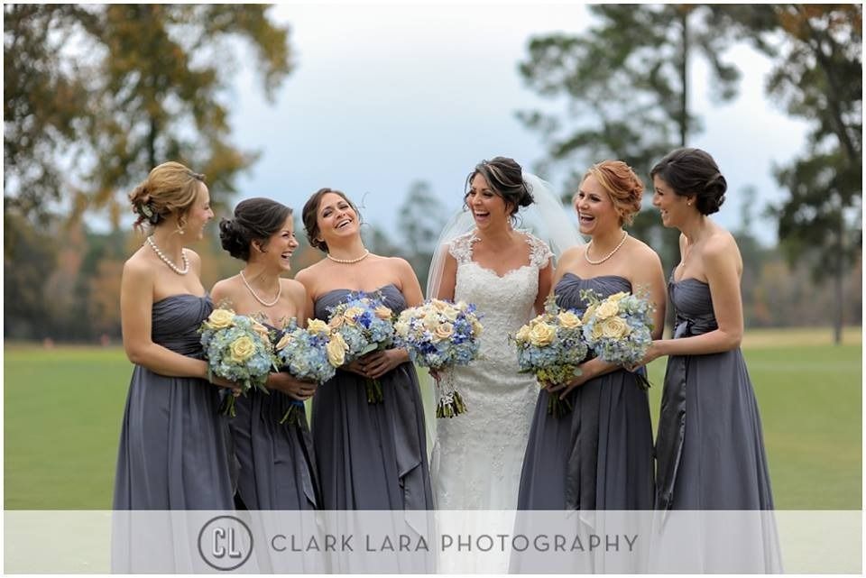Five women in gray dresses holding blue and white bouquets outdoors at a wedding