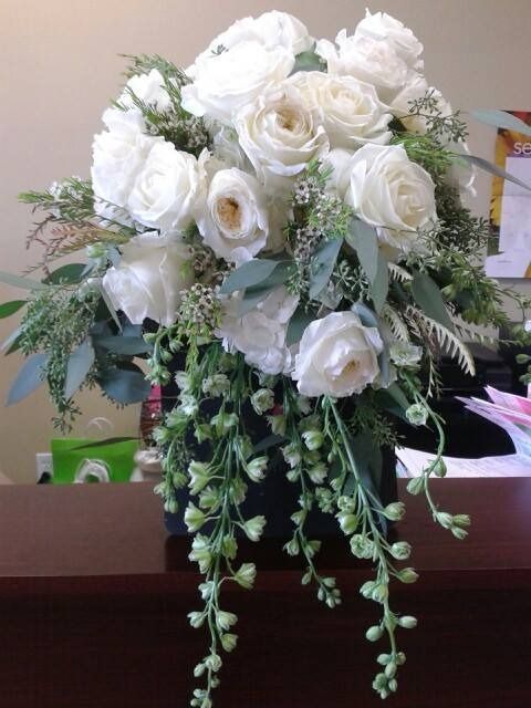White rose bouquet with trailing greenery in a vase on a table