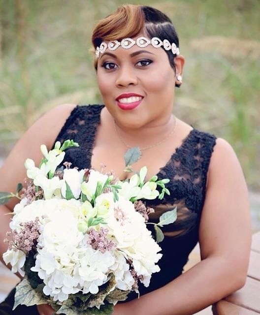 Woman in a black dress holding a large white bouquet, wearing a jeweled headband outdoors.
