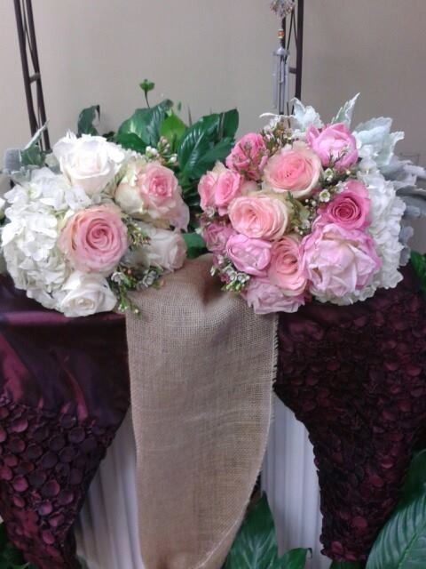 Two pastel rose bouquets in white and pink sit in a tall burlap-wrapped vase