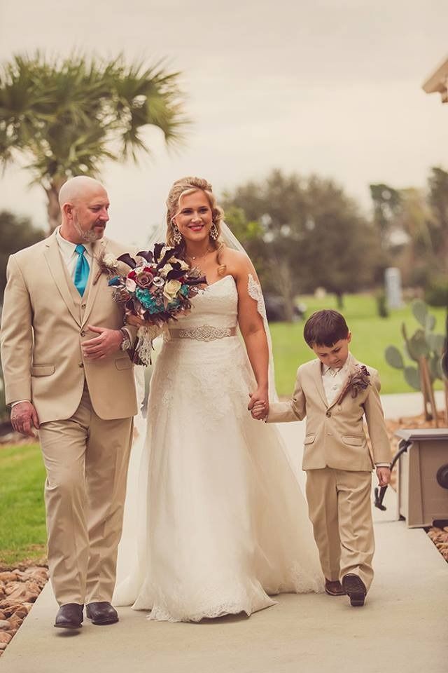 Wedding party walking outdoors, bride in white dress with bouquet, groom and young attendant in tan suits