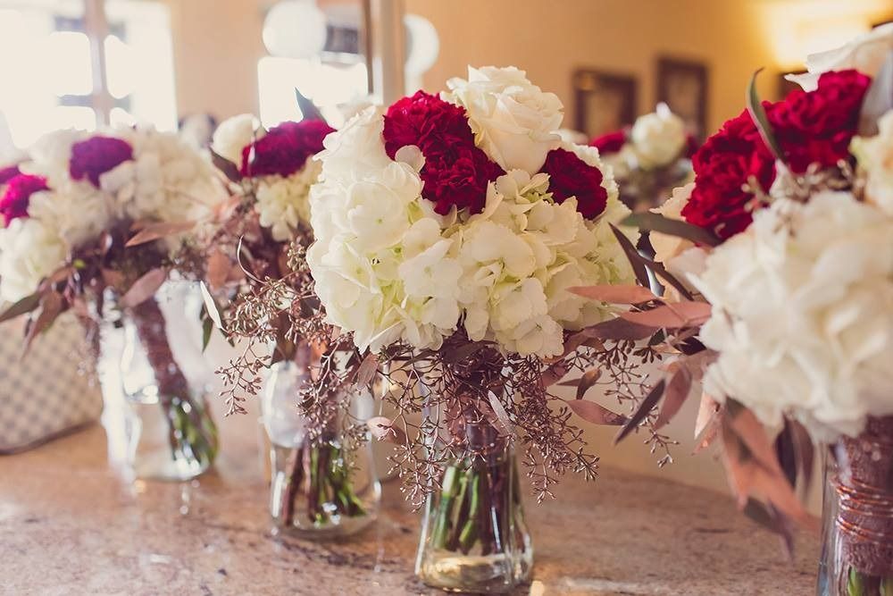 Glass jars of white and burgundy flowers arranged on a table in a bright room