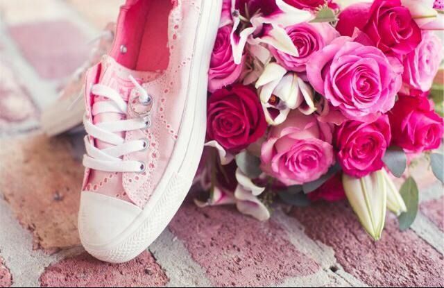 Pink sneaker beside a bouquet of pink roses on a rustic wooden surface