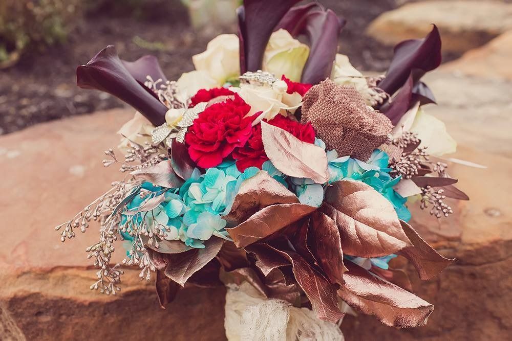 Bright bouquet of red, turquoise, and cream flowers with brown leaves on a rustic stone surface