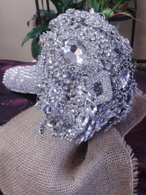 Silver rhinestone brooch on burlap fabric with a blurred plant in the background