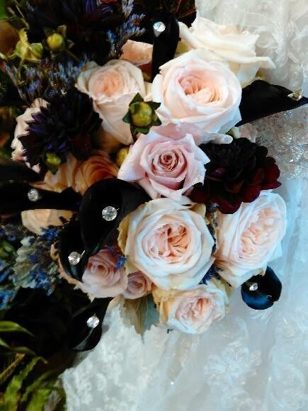 Bouquet of pale pink and white roses with dark accent flowers on a lace surface