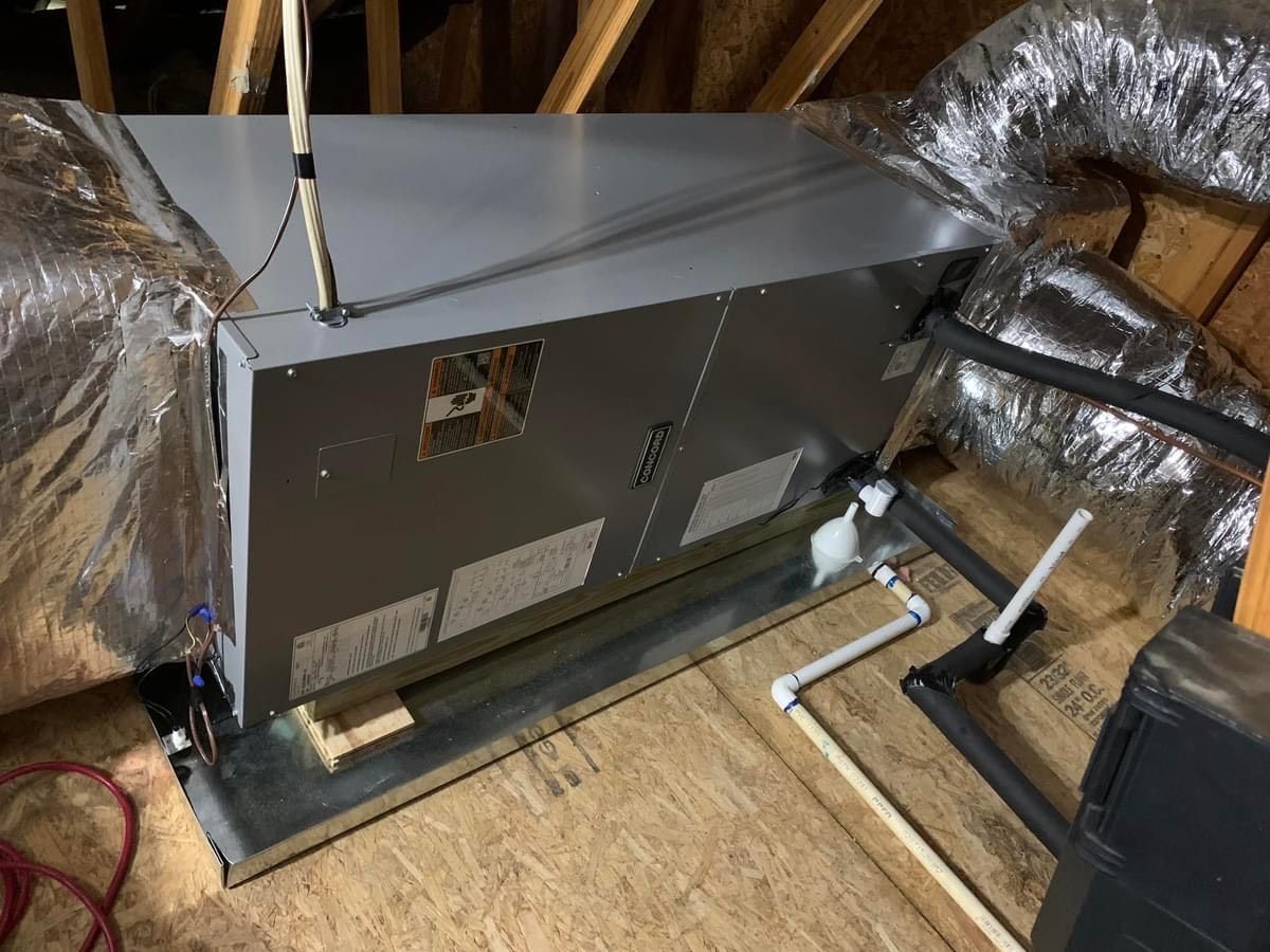 Attic HVAC unit with insulated ductwork and PVC pipes on a wooden floor