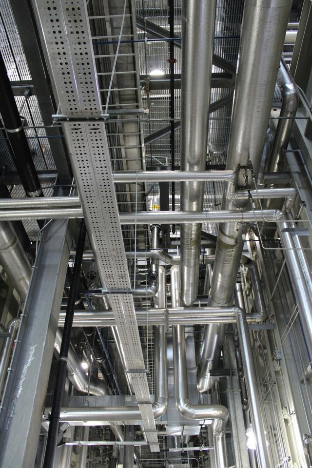 Industrial ceiling with dense metal pipes, ducts, and cable trays in a mechanical room