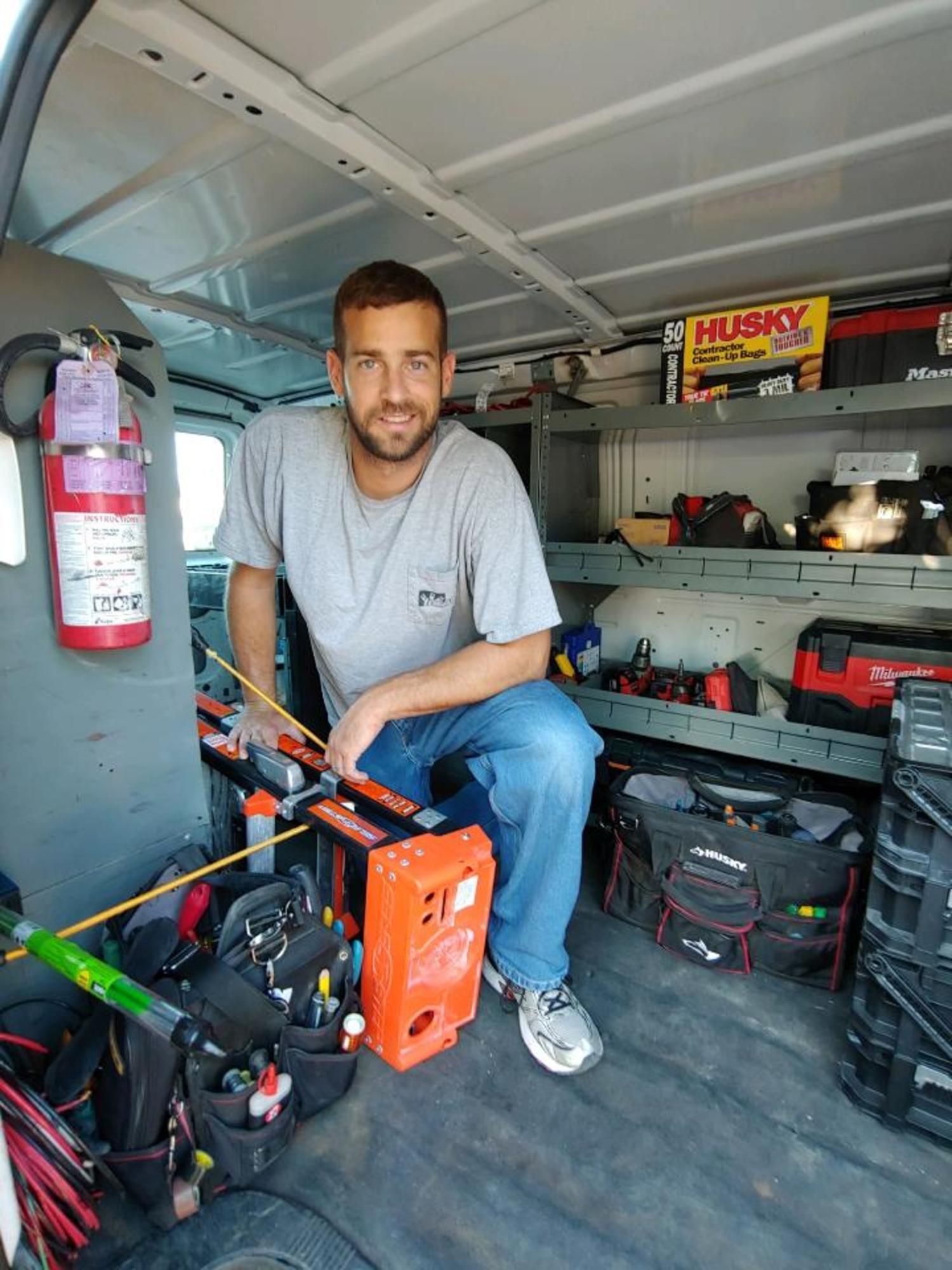A man is sitting in the back of a van filled with tools.