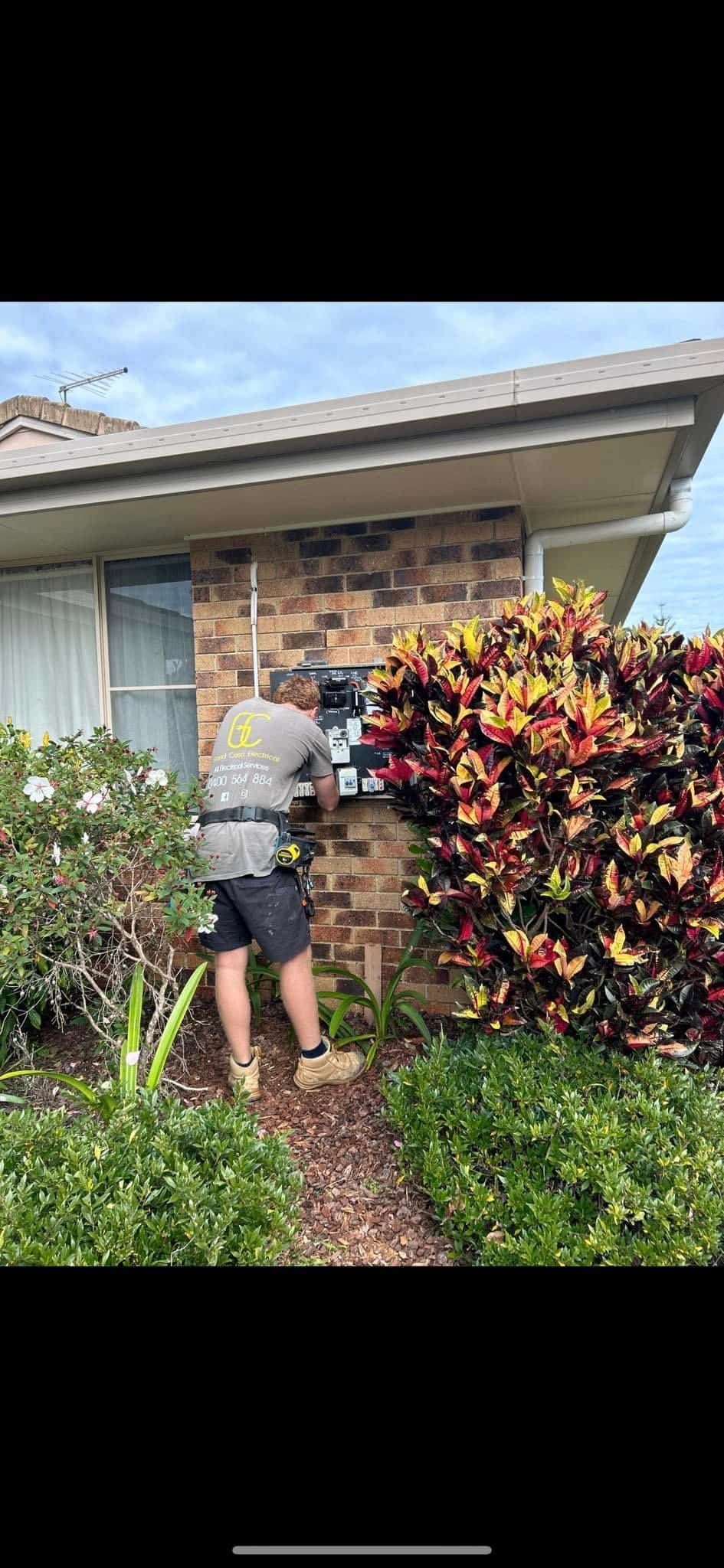 A Man Is Working On An Electrical Box In Front Of A House — Grand Casa Electrical Solar & Batteries In Byron Bay, NSW
