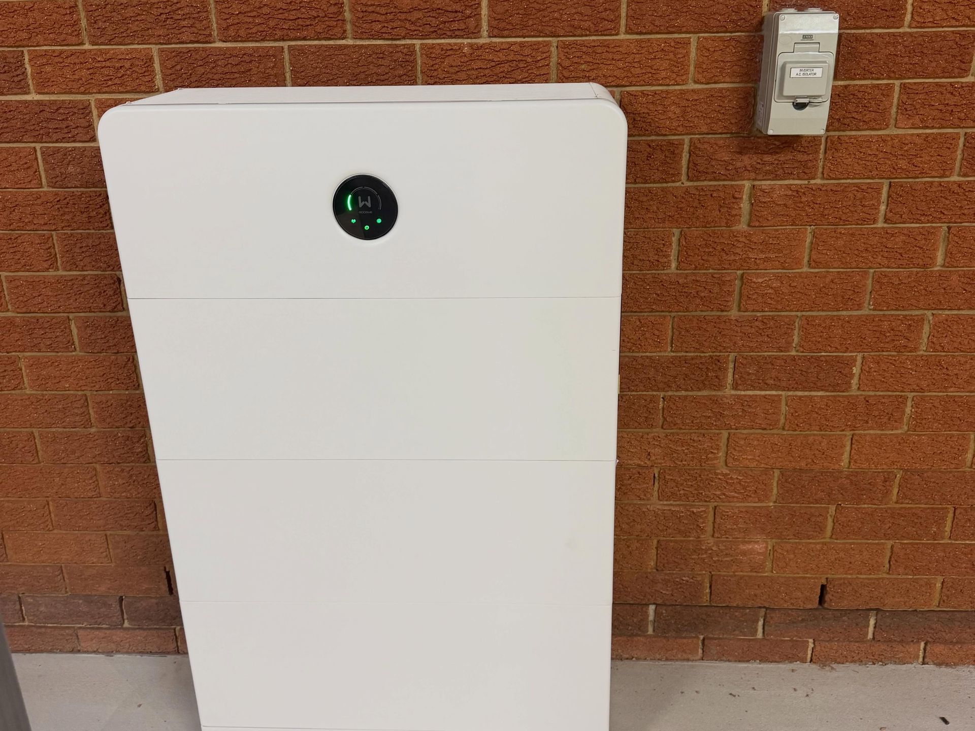 White Wall-mounted Cabinet With a Small Round Display on a Brick Wall Outside — Grand Casa Electrical Solar & Batteries In Northern Rivers, NSW