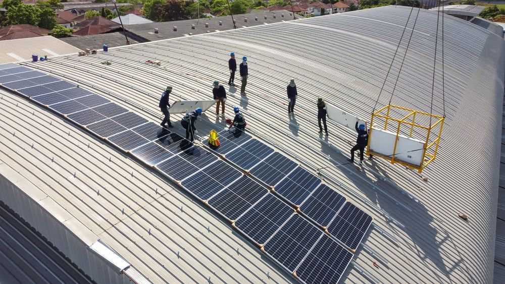 A Group Of People Are Installing Solar Panels On The Roof Of A Building — Grand Casa Electrical Solar & Batteries In Ballina, NSW