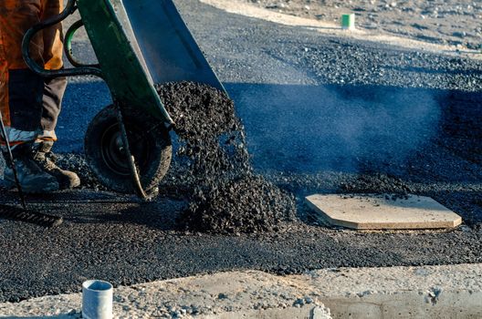 Worker pouring black asphalt from a paver onto a road during paving work