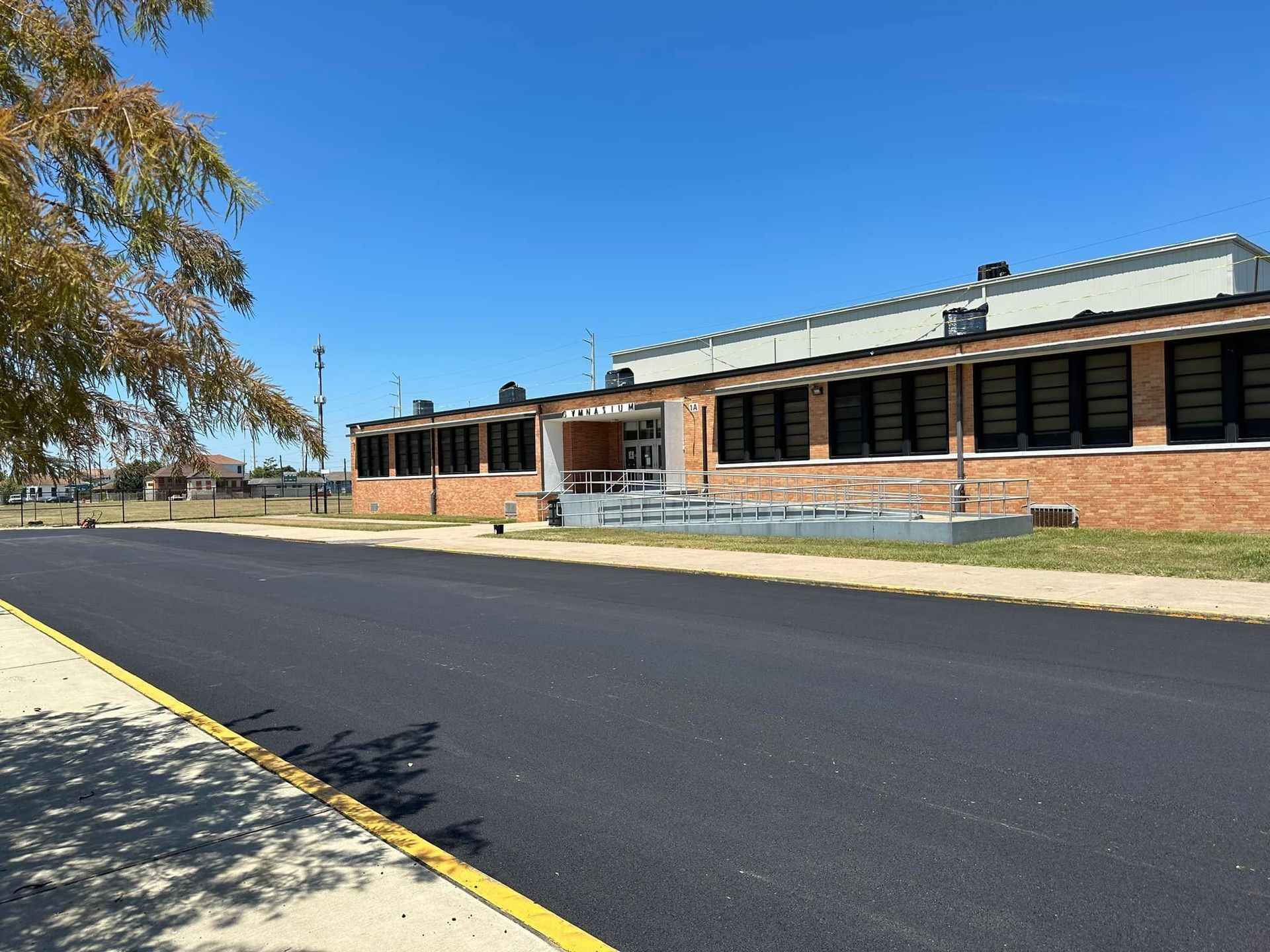 Single-story brick building with dark windows beside a paved road on a sunny day