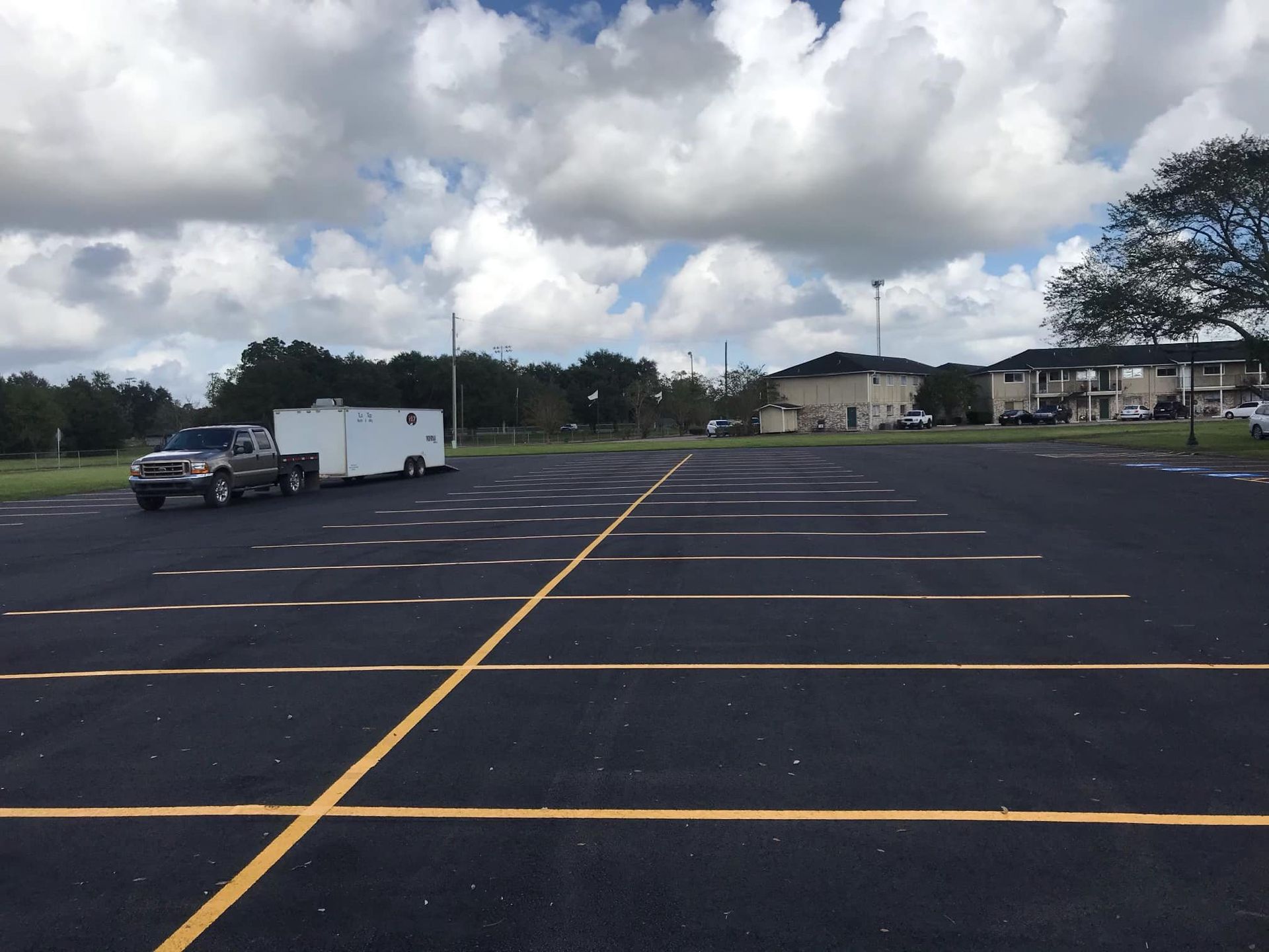Empty parking lot with yellow lines, a few parked vehicles, and cloudy sky