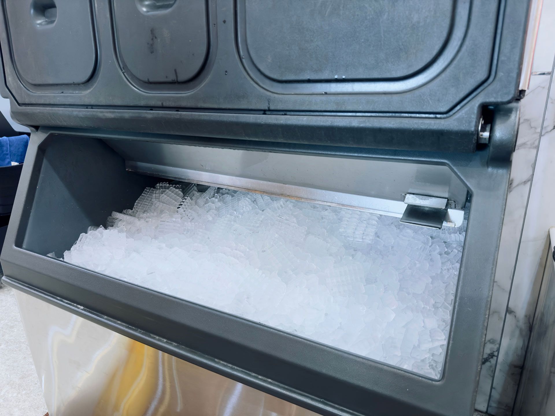 Ice machine bin filled with crushed ice; stainless steel and gray exterior.