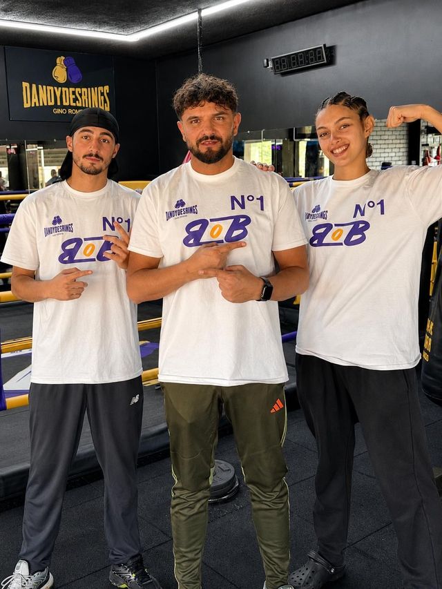 Trois personnes vêtues de maillots blancs et bleus « N°1 » posent à l’intérieur, un verre à la main.