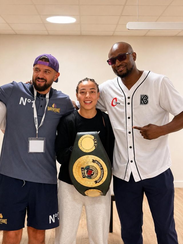 Trois personnes posent en intérieur, tenant une ceinture de champion, souriant à l'objectif.