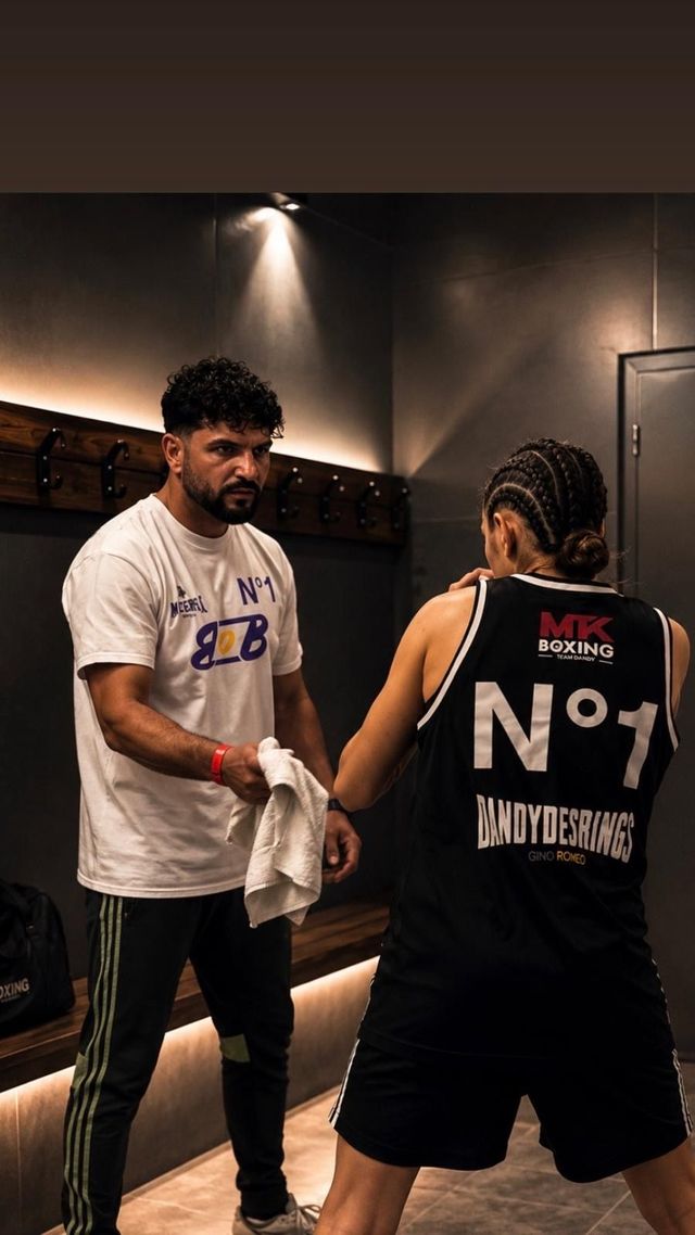 Deux personnes s'entraînent avec des paos de boxe, vêtue d'un débardeur noir.