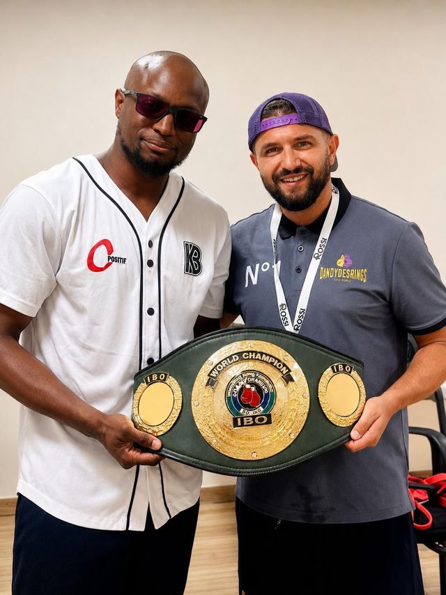 Deux hommes posent avec une ceinture de champion, souriant à l'intérieur.