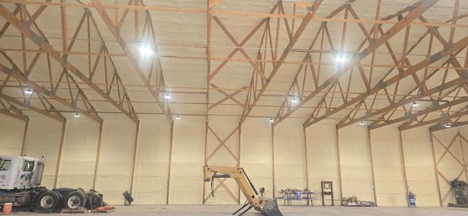 Large empty warehouse interior with exposed trusses, hanging lights, and construction equipment near the walls