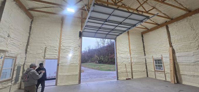 Inside a warehouse, two people stand by a door near an open loading bay with a view outside.