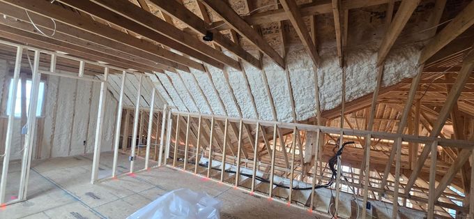 Framed attic under construction with exposed wooden rafters, white wall panels, and insulation on the floor