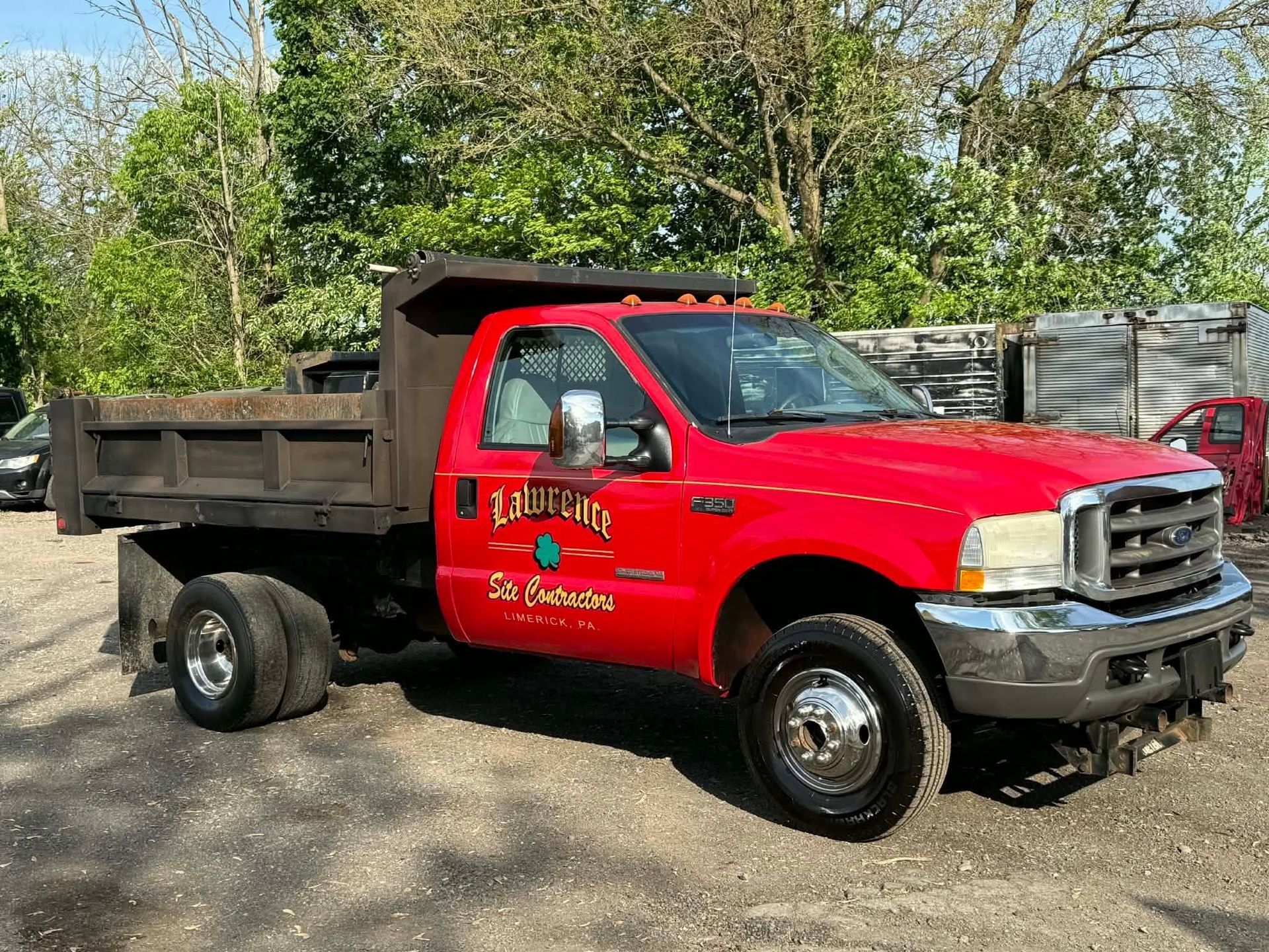 Red dump truck parked on a dirt lot with trees and fencing in the background