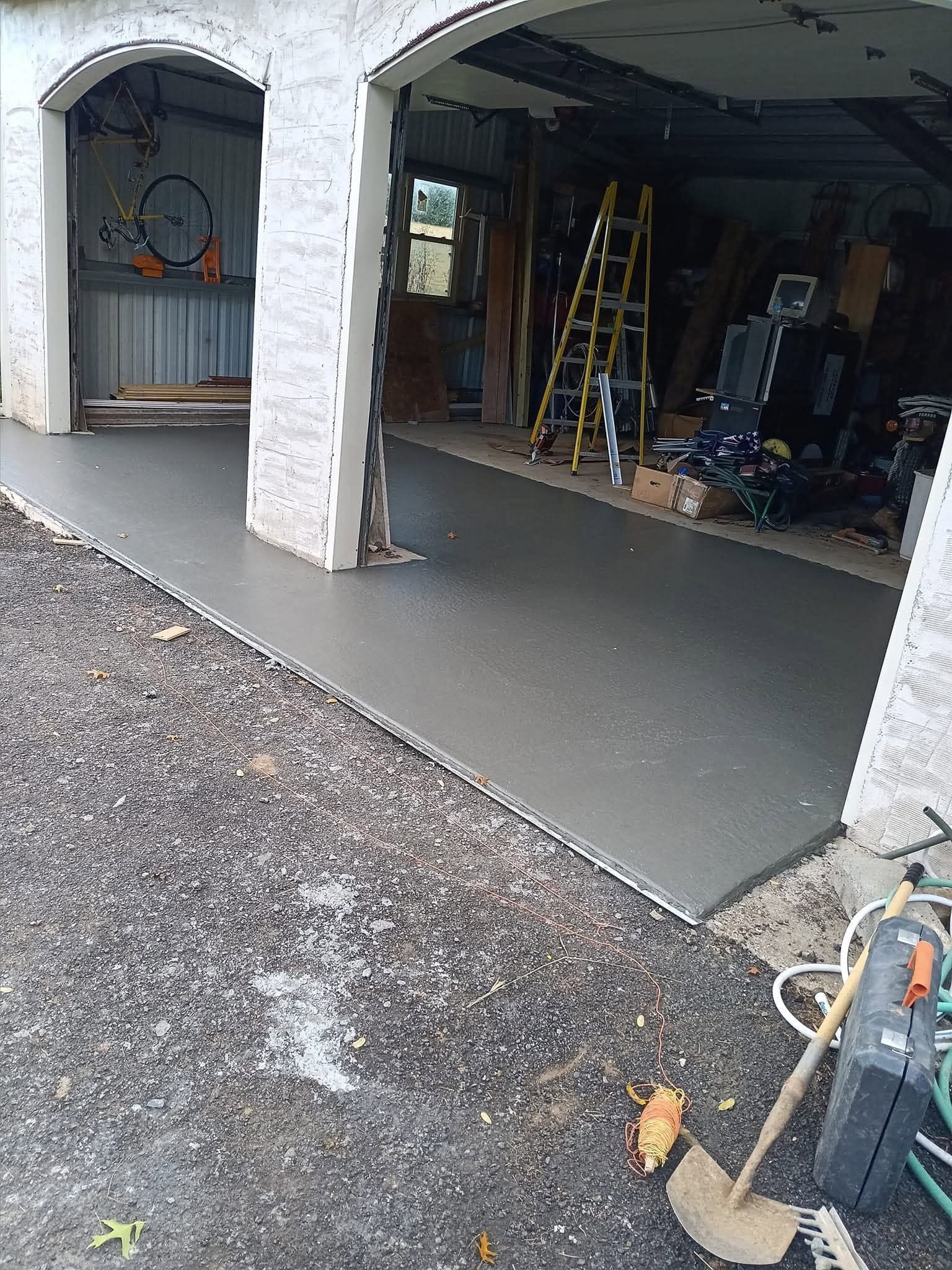 Partially finished concrete garage floor with tools and ladders inside a two-bay workshop