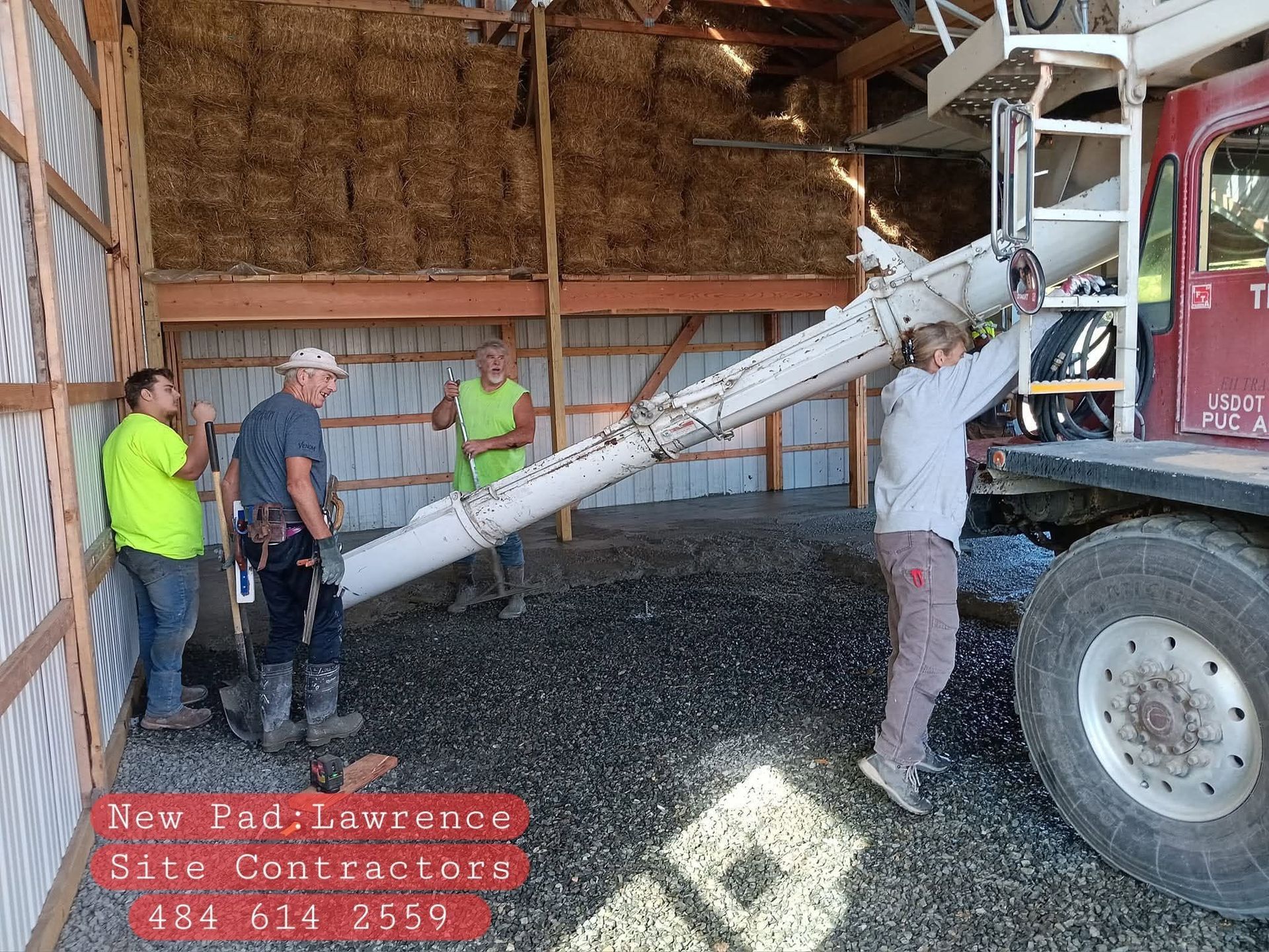 Workers unloading dark gravel from a truck into a barn with a conveyor chute