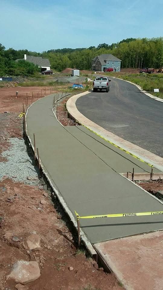 Curved concrete sidewalk under construction beside a paved road, with a car in the distance.