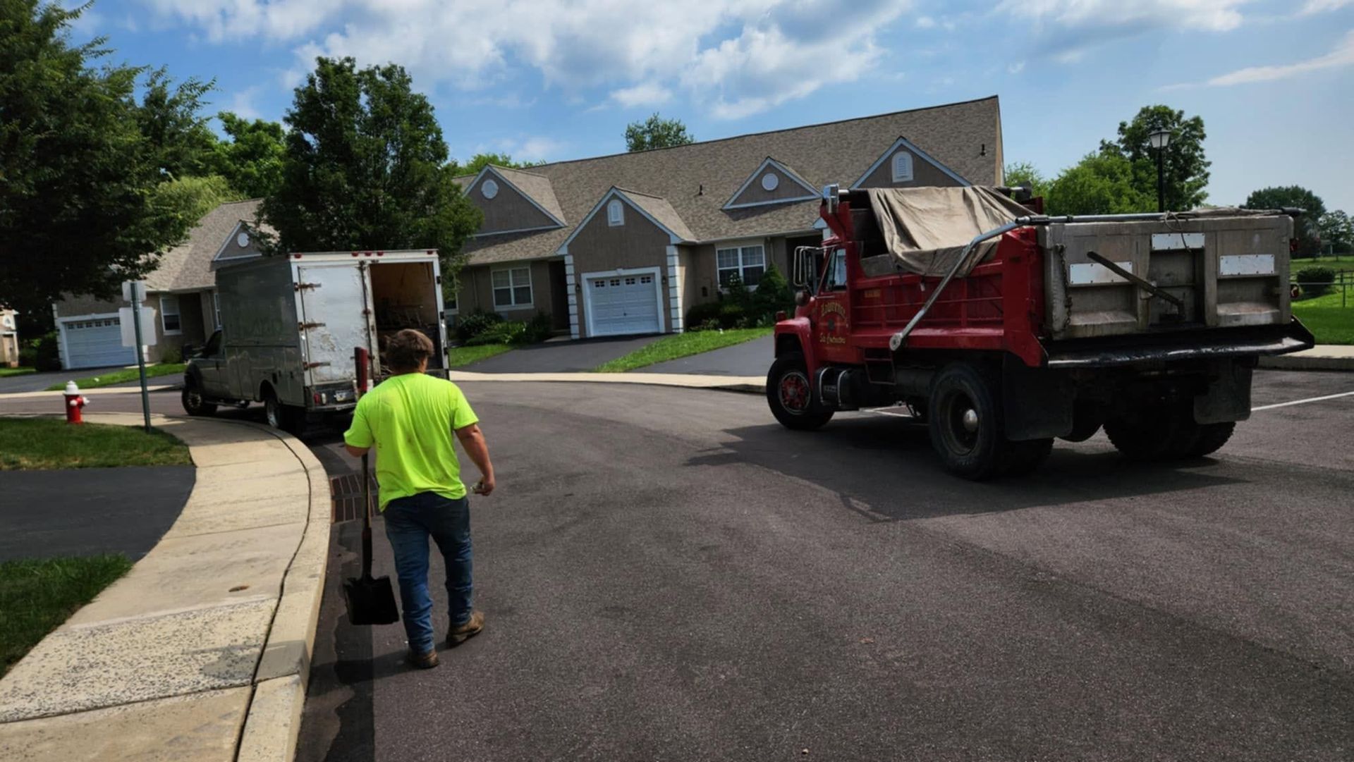 Worker pushing a black trash bin toward a red dump truck on a suburban street.