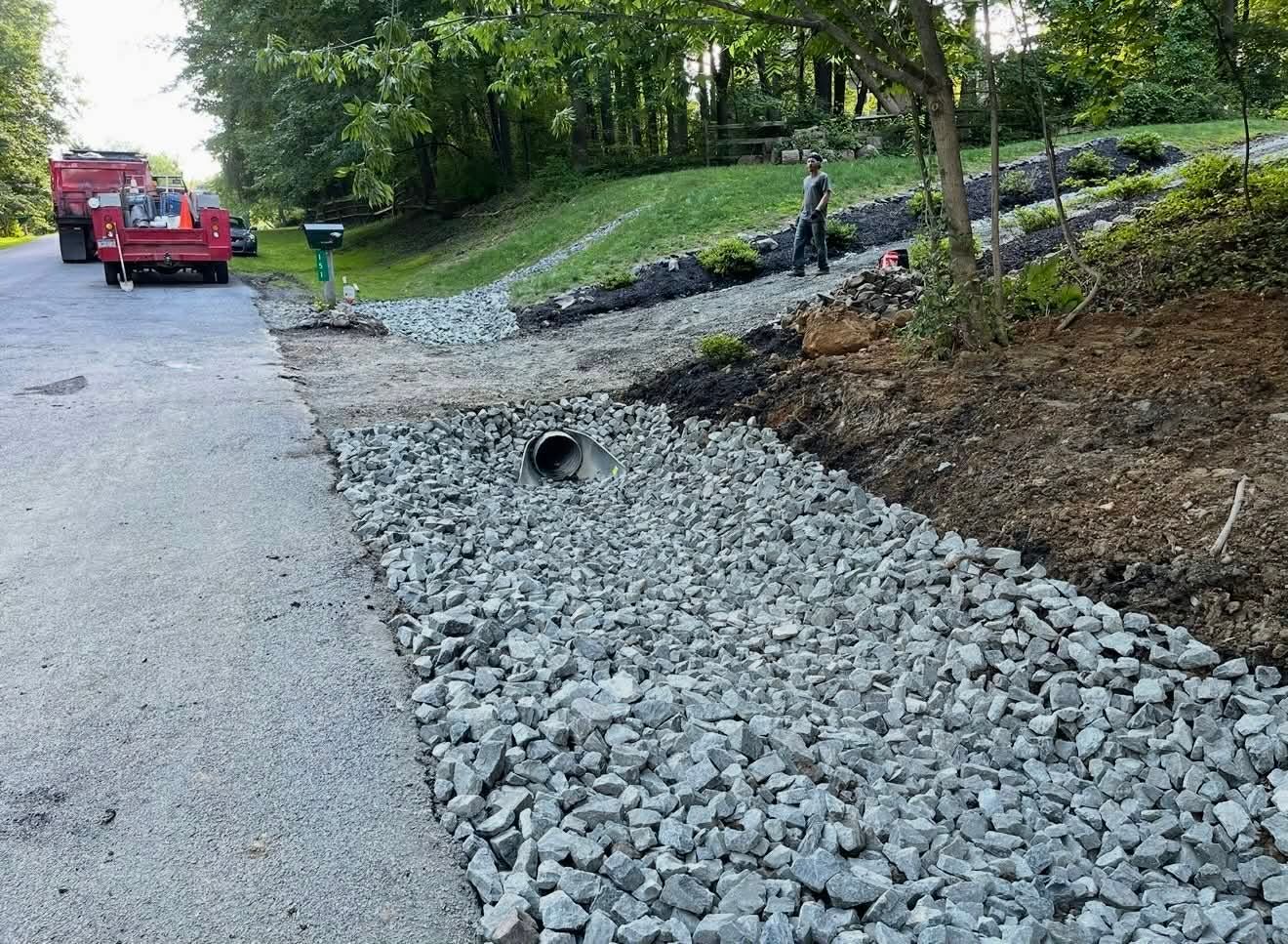 Rock drainage trench beside a road, with a red truck and worker in the background.