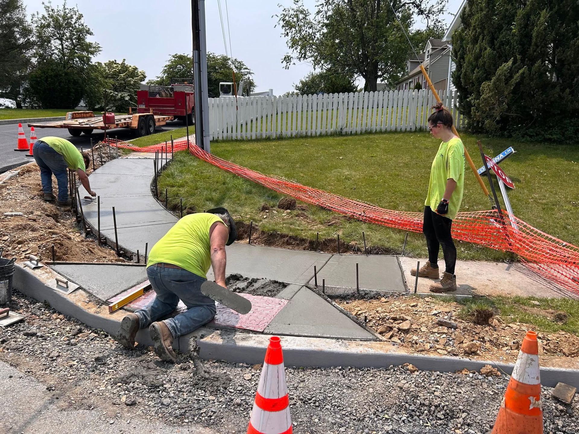 Workers in neon vests install a concrete curb at a roadside construction site.