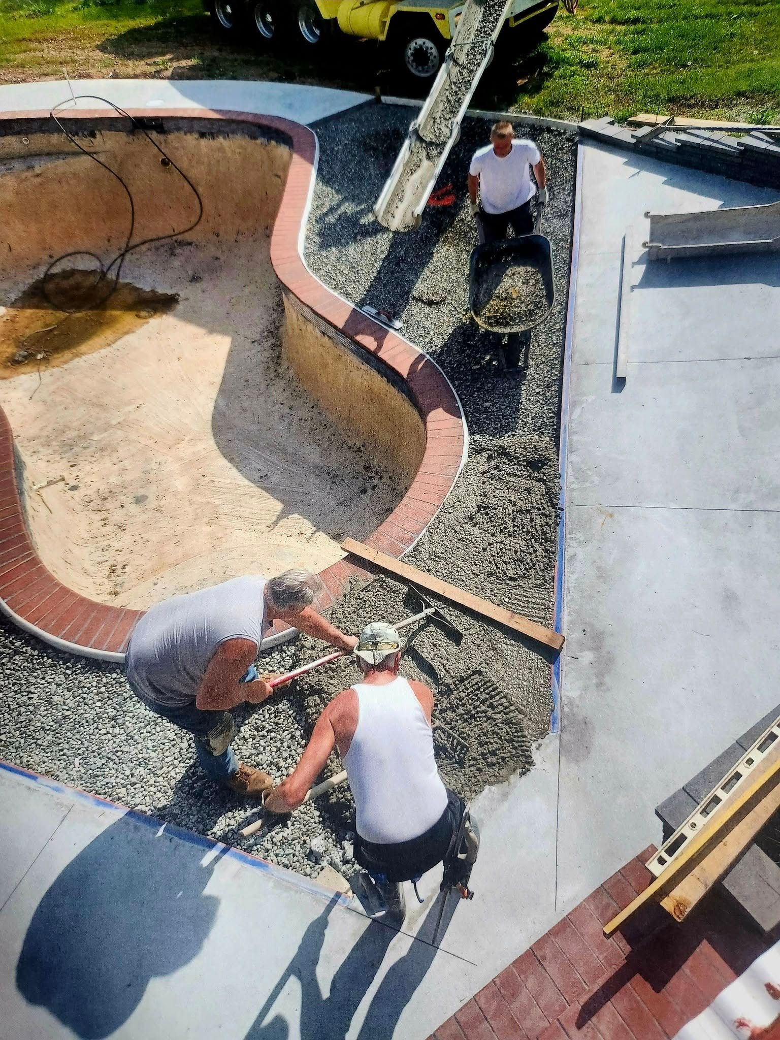 Workers installing gravel and edging around a small backyard pool under construction