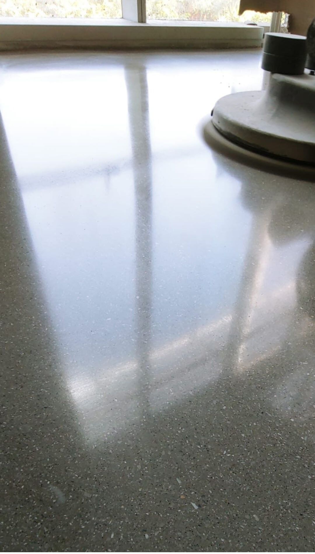 Reflective gray countertop with a window reflection and a round appliance base on the right