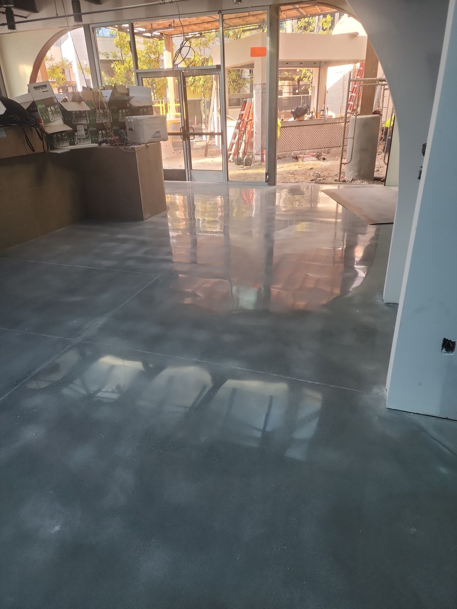 Empty sunlit room with polished concrete floor and large arched windows.