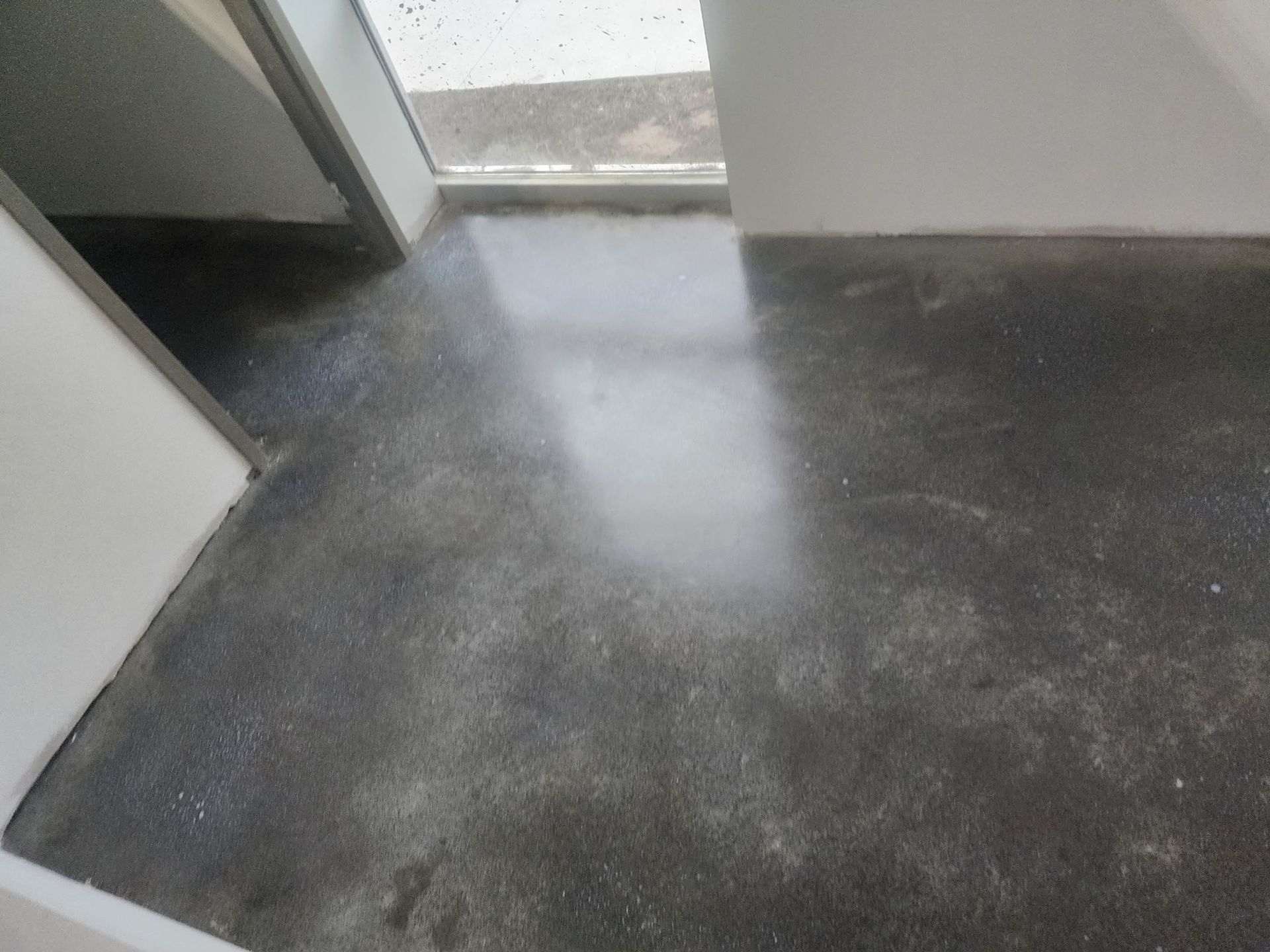 Empty dark floor with a bright white spill or stain near a doorway.