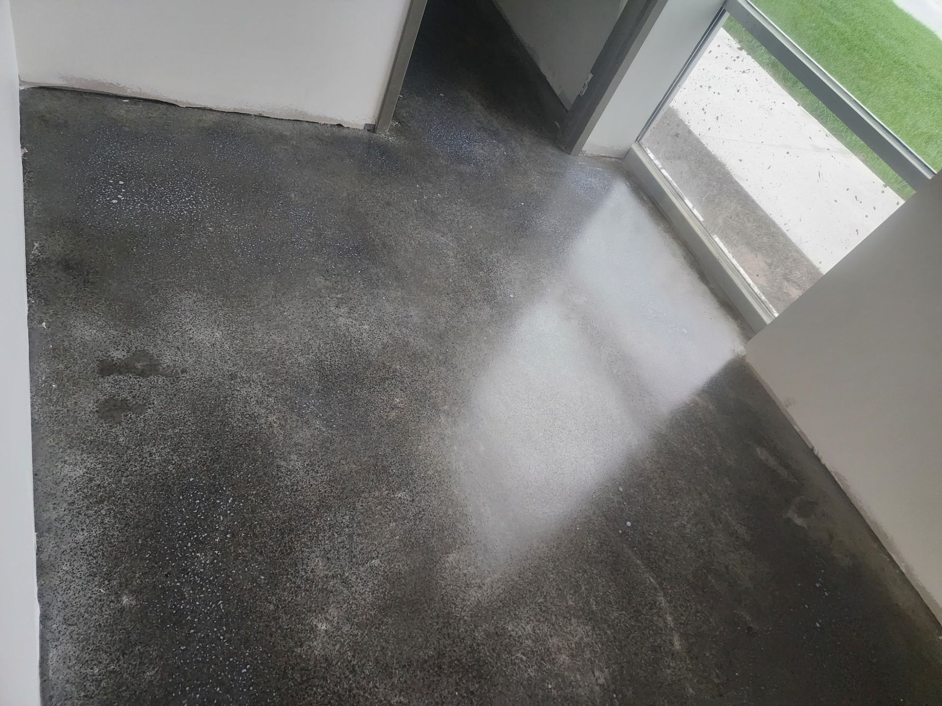 Dark speckled floor by a doorway and window, with a bright patch of light on the surface