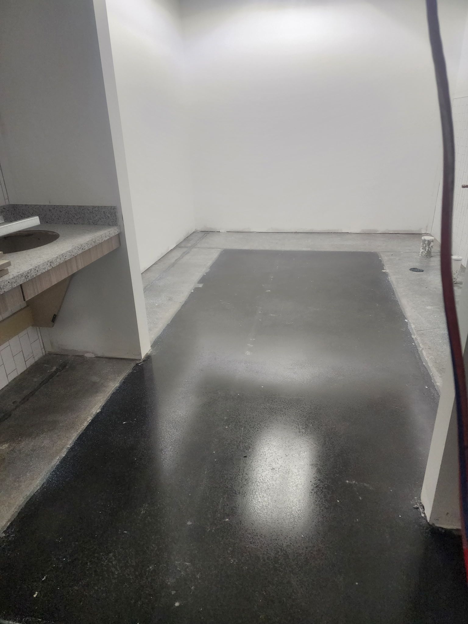 Empty room with glossy black floor, white walls, and built-in shelving on the left.