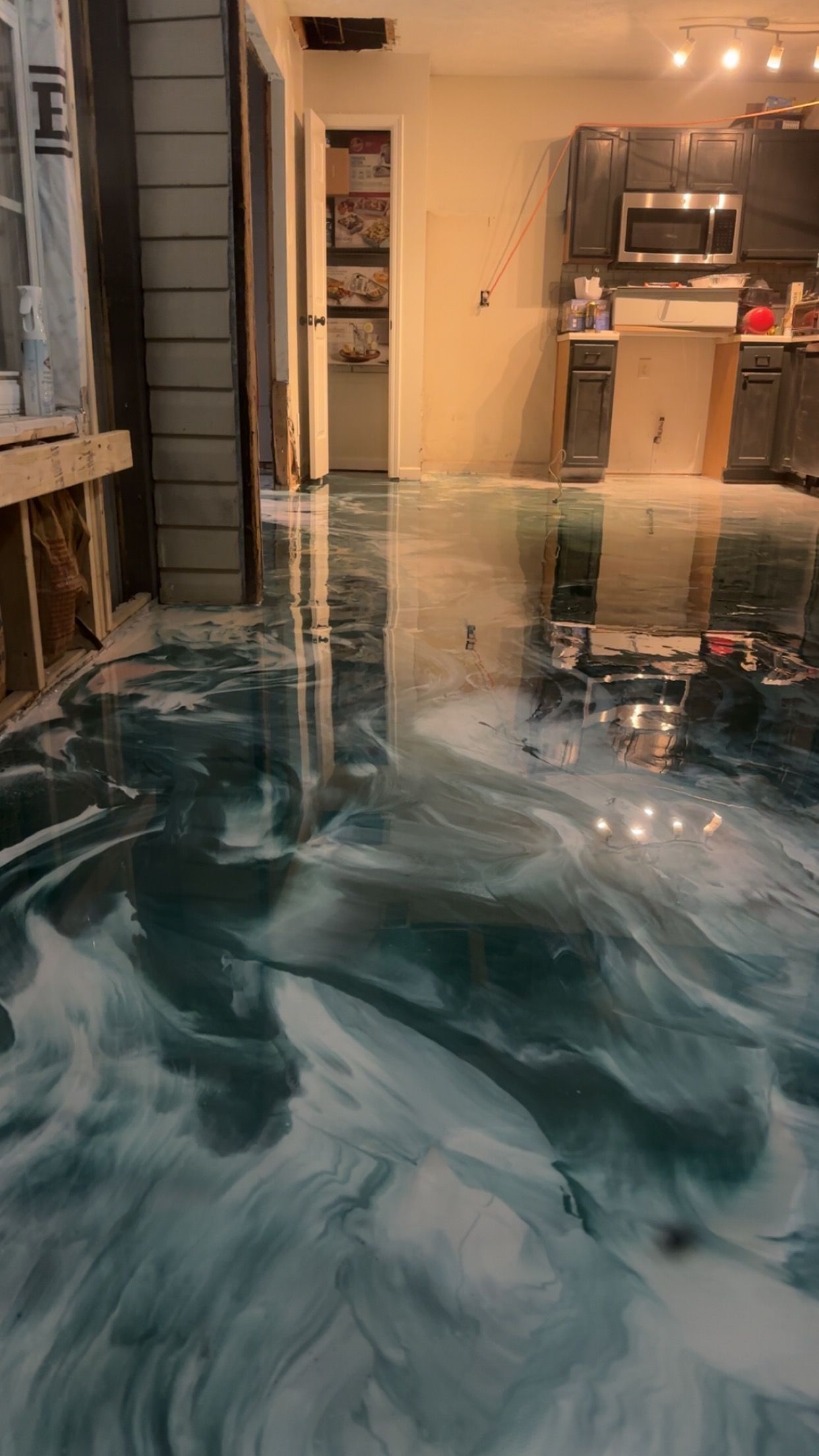 Flooded home interior with water covering the floor and swirling foam near a kitchen and hallway.