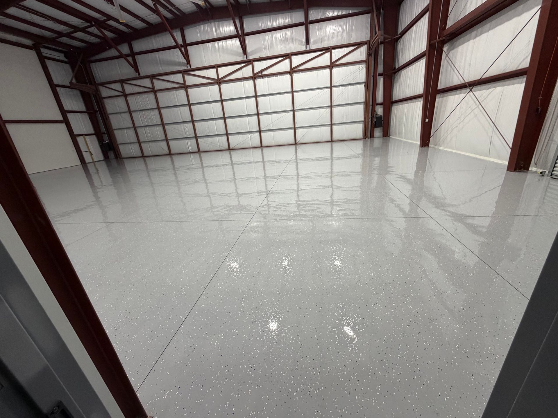 Empty warehouse with a glossy gray epoxy floor and red steel walls and beams.