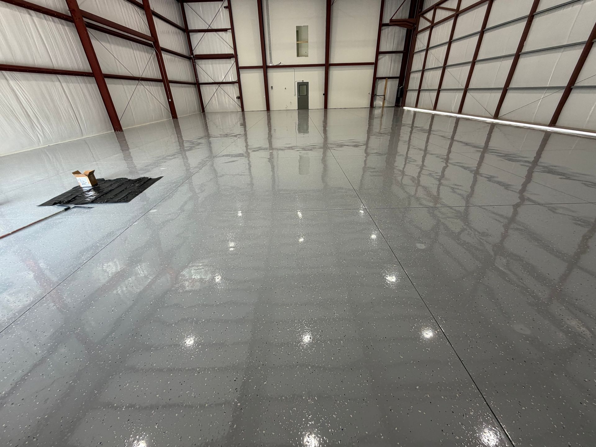 Empty warehouse with a glossy gray floor reflecting the ceiling lights and beams