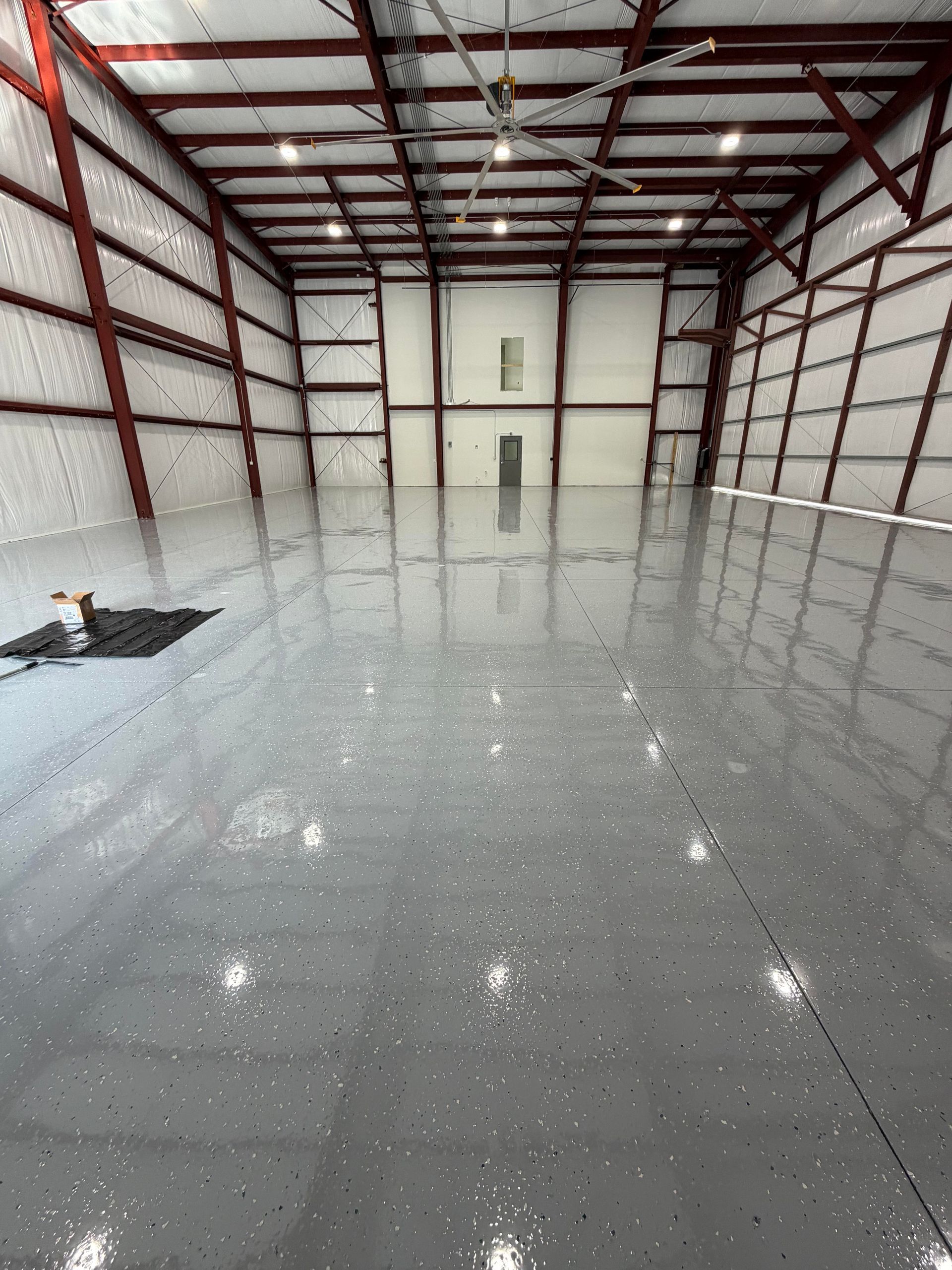 Empty industrial warehouse with a glossy gray floor and red steel roof beams.