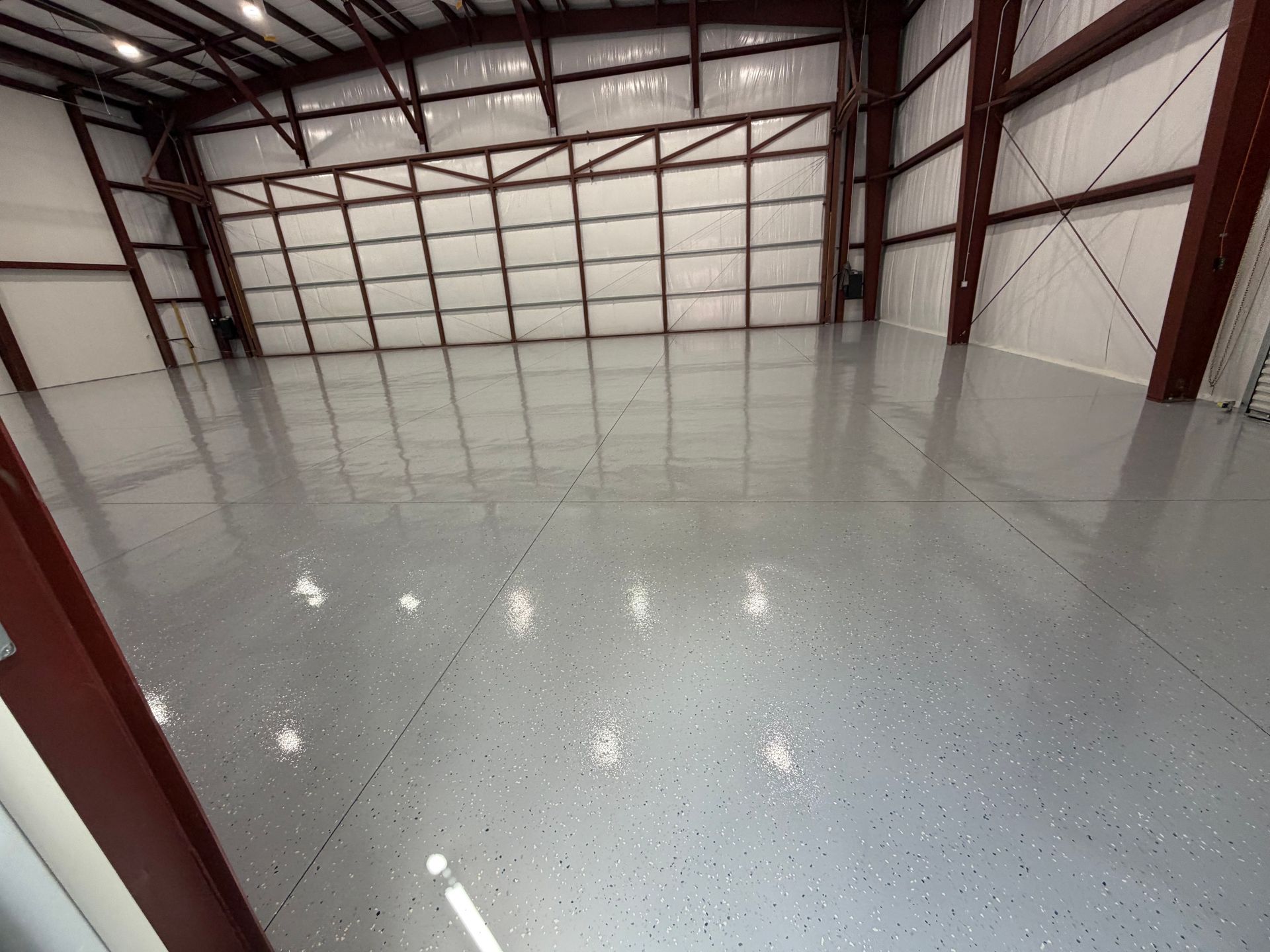 Empty warehouse interior with glossy gray epoxy floor and red steel beams along the walls and ceiling