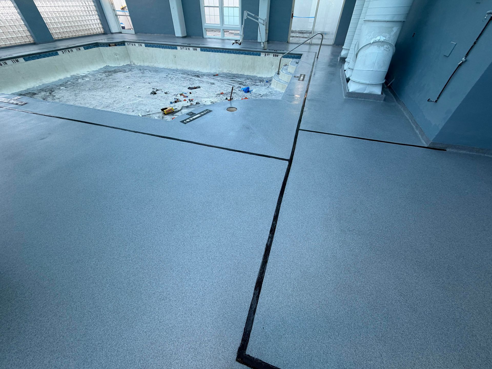 Rooftop deck with gray surface, a rectangular opening, and pipes near a building wall